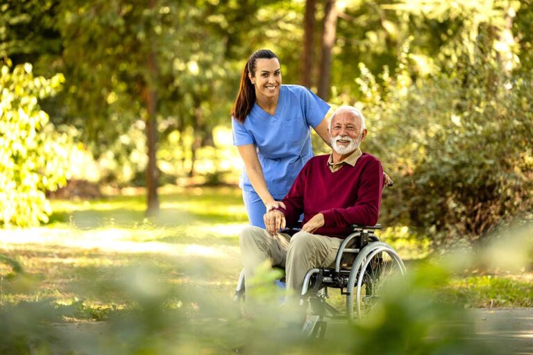 A caregiver assists an older adult in a cheerful common room with soft lighting and comfortable furnishings.